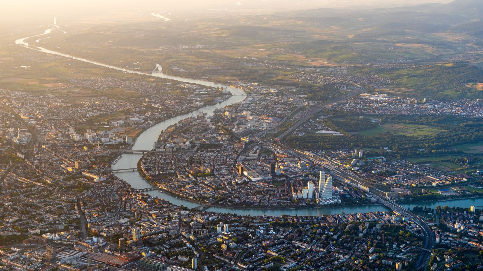Luftaufnahme von Basel im Abendlicht, der Rhein zieht sich durch die Stadt.